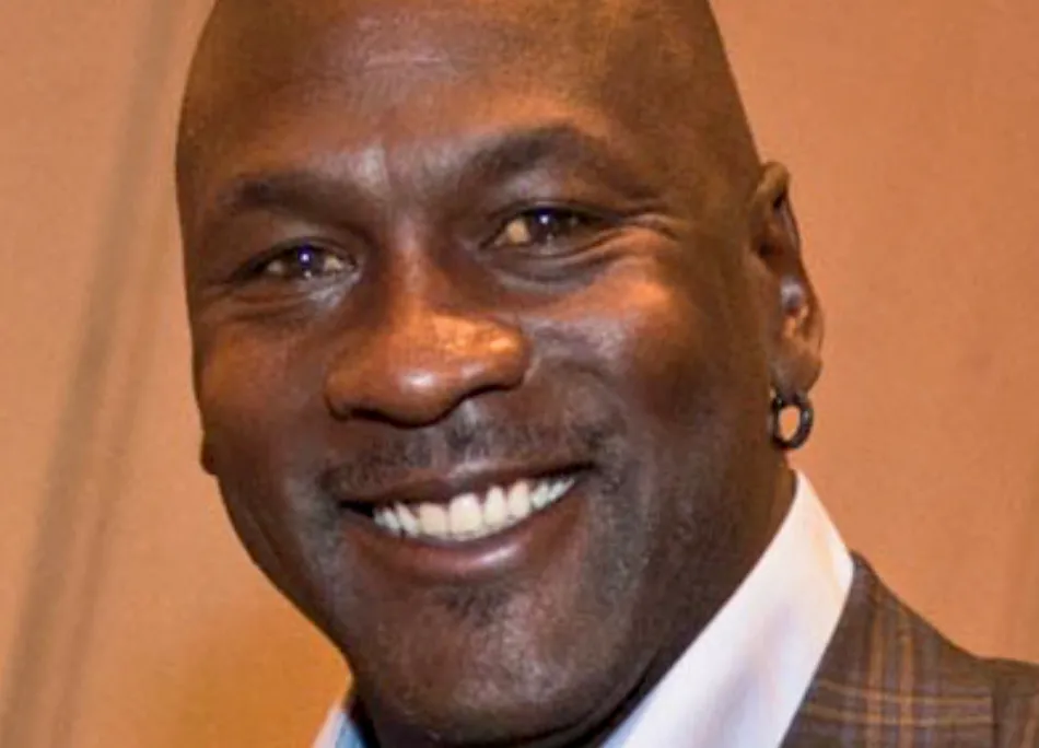 Close-up of Michael Jordan smiling, showing his white teeth and a hoop earring, against a brown background.
