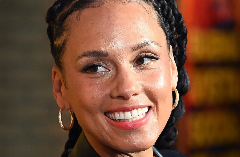 Close-up of Alicia Keys smiling, wearing gold hoop earrings with small diamonds, and braided hair.