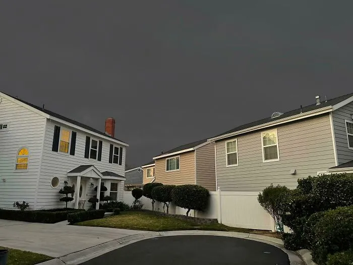 Suburban houses under a deeply unsettling dark, overcast sky, creating a liminal space.