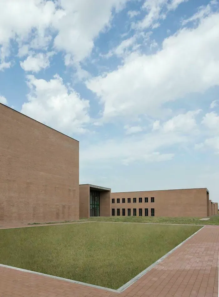 An unsettling liminal space showcasing a deserted modern brick building with sparse windows and a vast, empty lawn, an abyss of architecture.