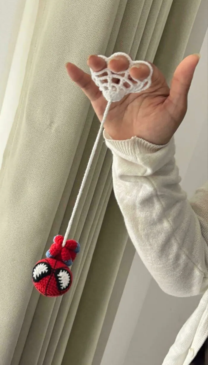 Hand holding crocheted toy spider hanging from yarn web