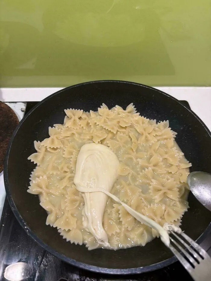Bowtie pasta cooking in a pan with a large clump of melted cheese, an unappetizing food combo.