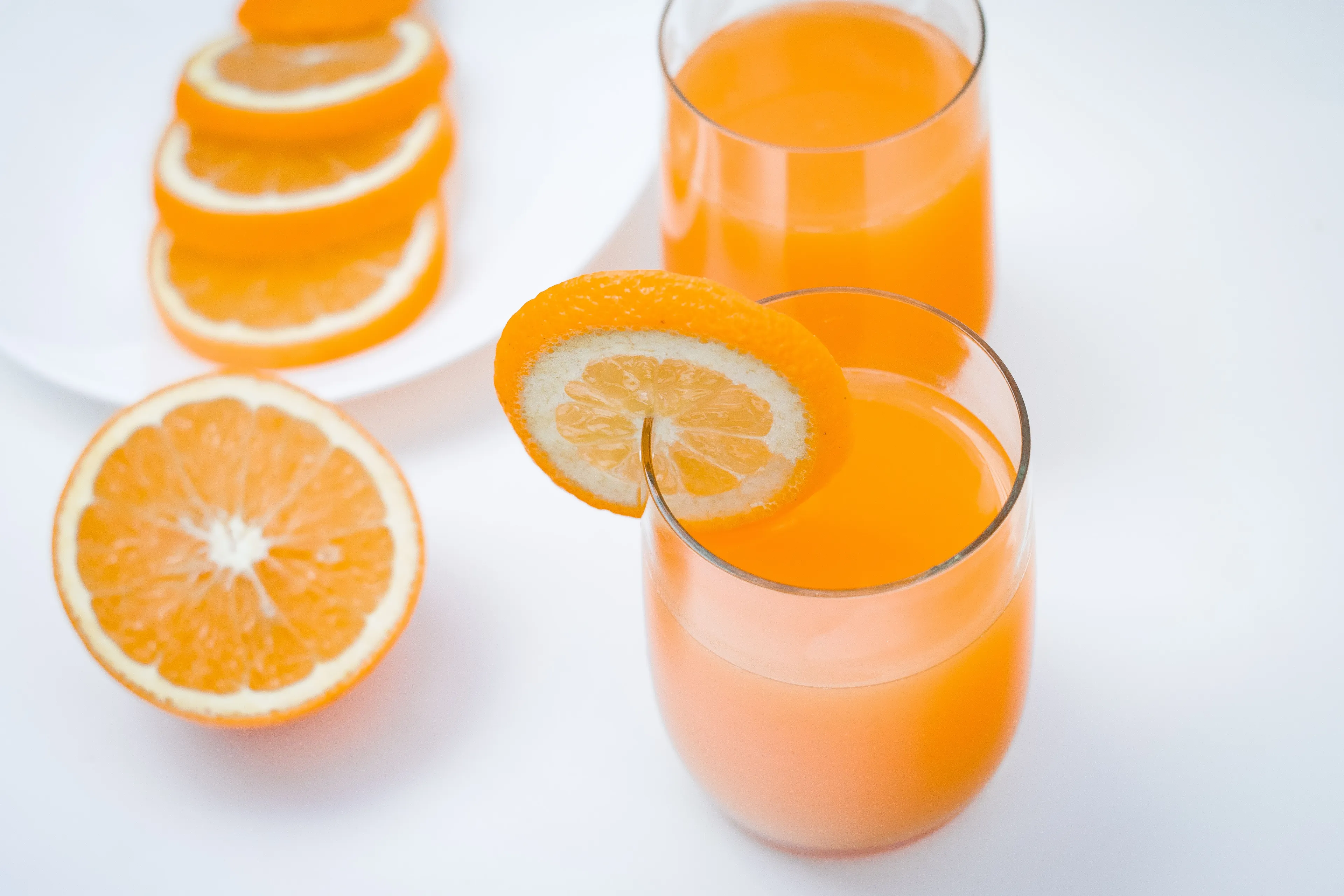 Two glasses of refreshing orange juice with orange slices on the rim, a delicious comfort drink.