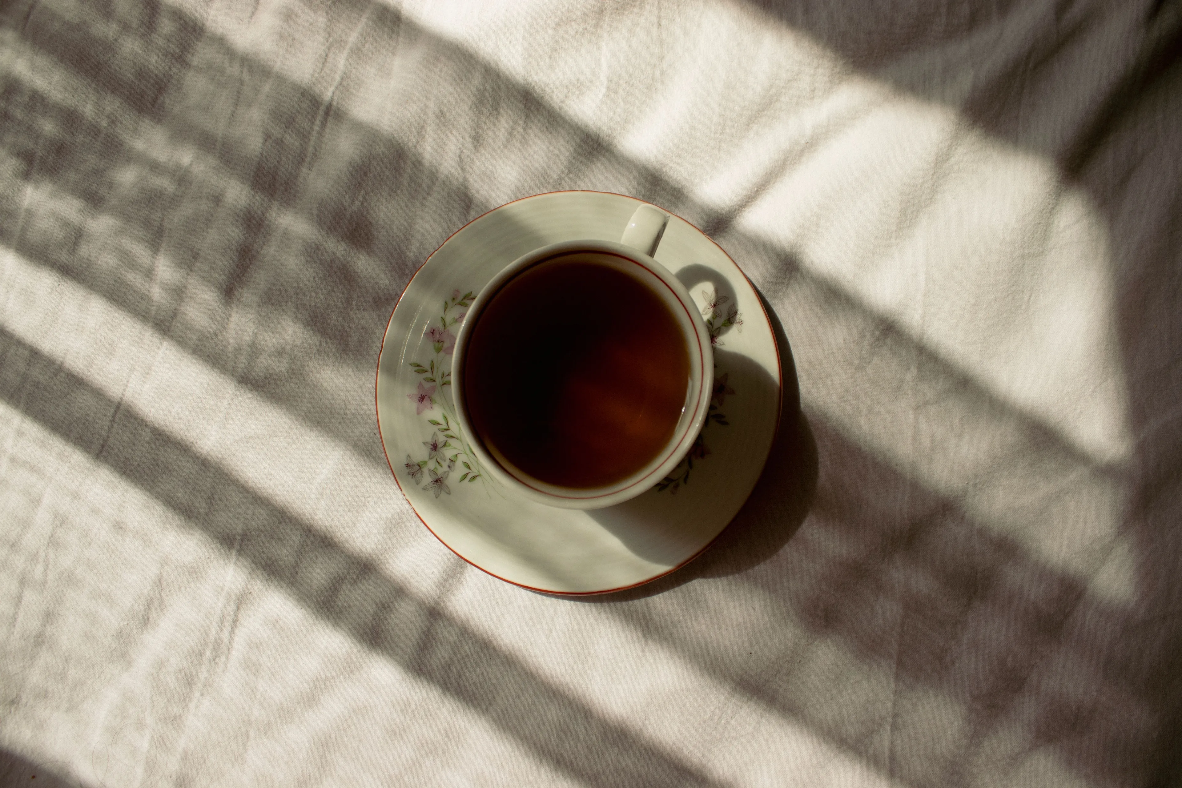 A comforting cup of tea, with sunlight streaming through blinds, on a white tablecloth.
