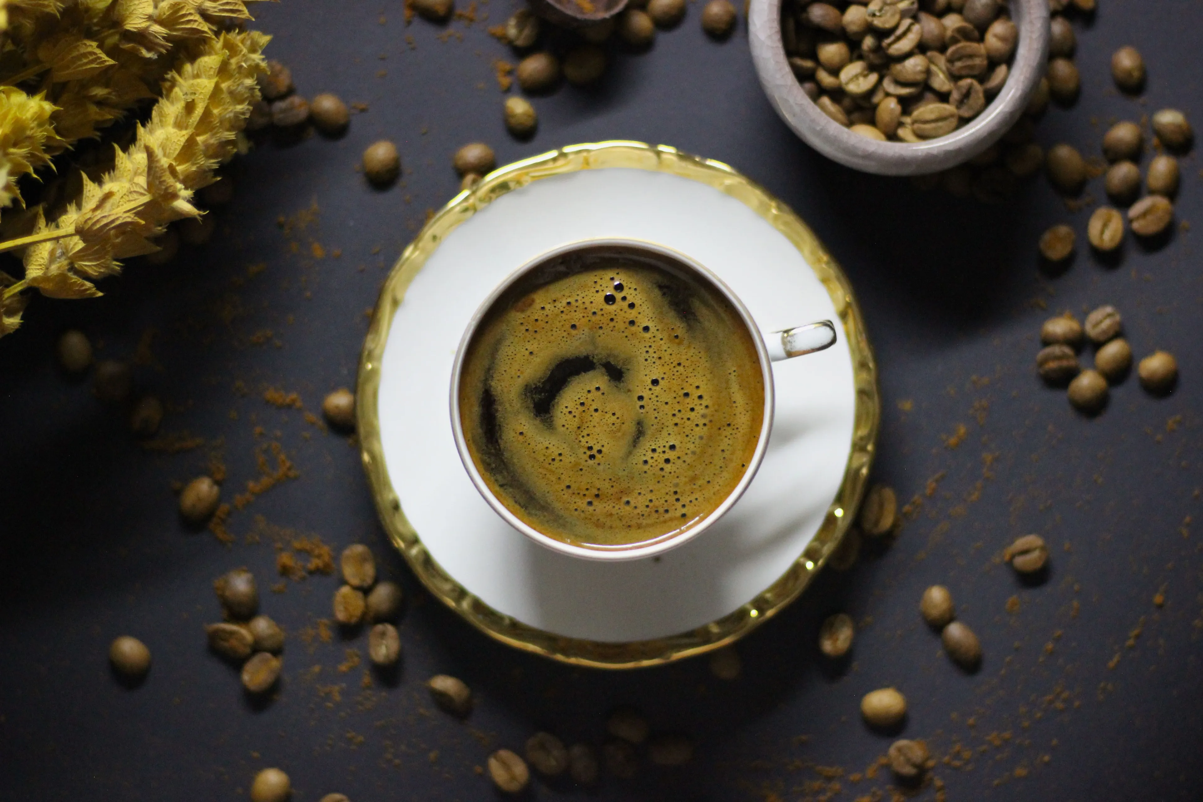 Overhead view of black coffee in a white and gold cup, surrounded by coffee beans and spices.