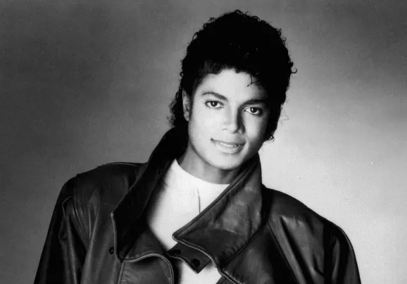 Michael Jackson, the King of Pop, smiling in a black and white studio portrait wearing a leather jacket.