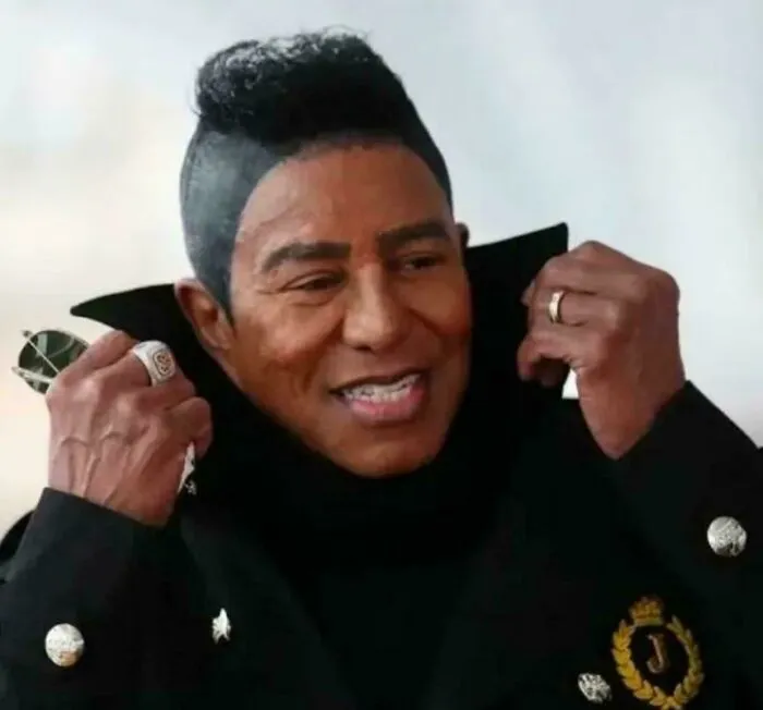 Man with unfortunate haircuts, styled with a distinct faux hawk and shaved sides, smiling.