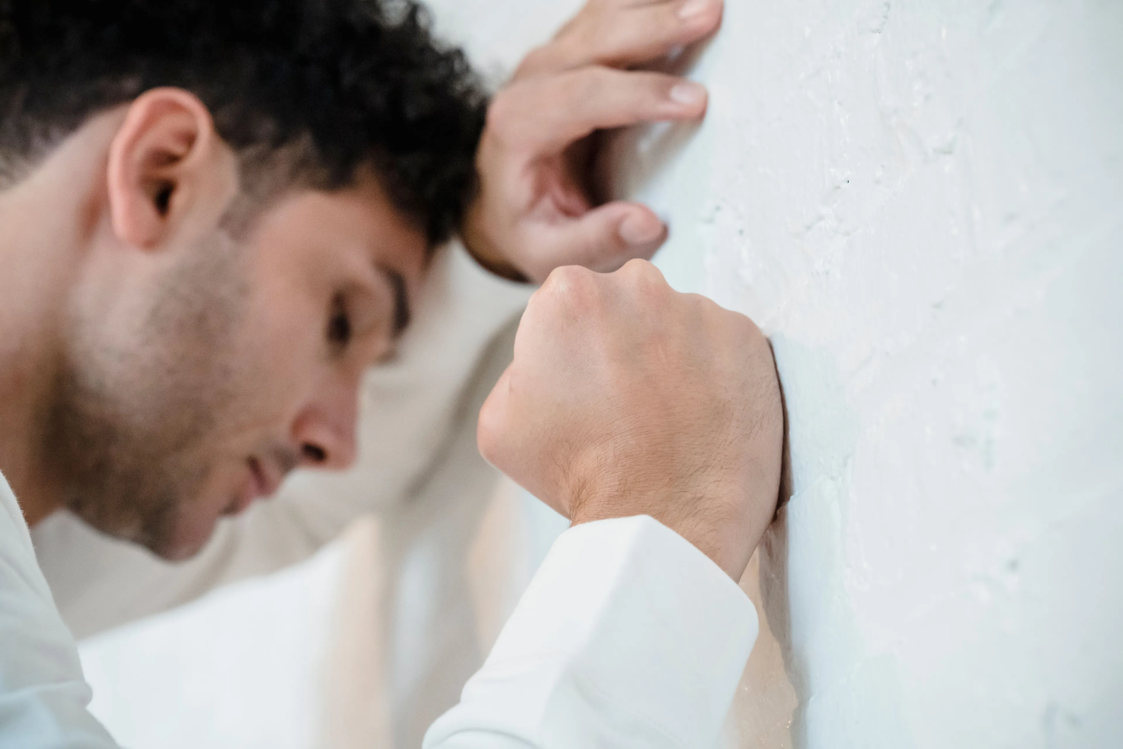 A man leans against a wall with a clenched fist, showing frustration and the fear of failure.