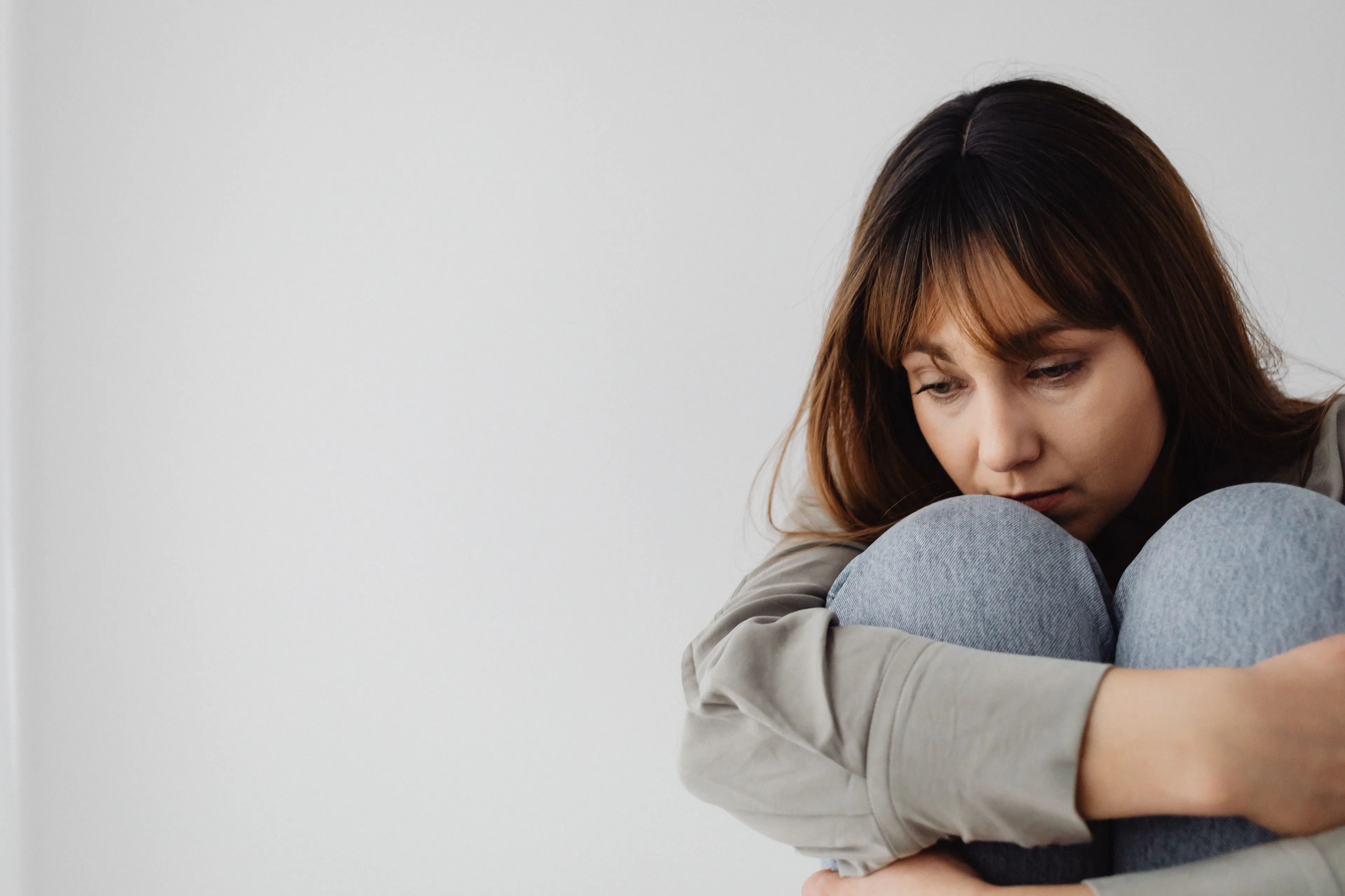 A woman sits with her knees to her chest, appearing withdrawn and vulnerable, representing the fear of vulnerability.