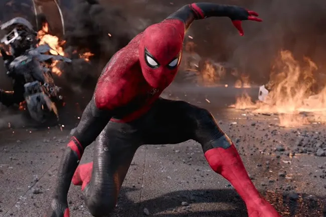 Spider-Man in his black and red suit crouches in a ruined street with explosions in the background.