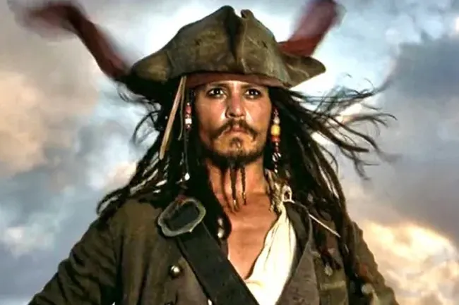 Jack Sparrow, a pirate with dreadlocks and a tricorn hat, looks directly at the viewer with a dramatic sky behind him.