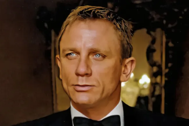 James Bond, in a tuxedo and bow tie, looks intently to his right with a blurred background.