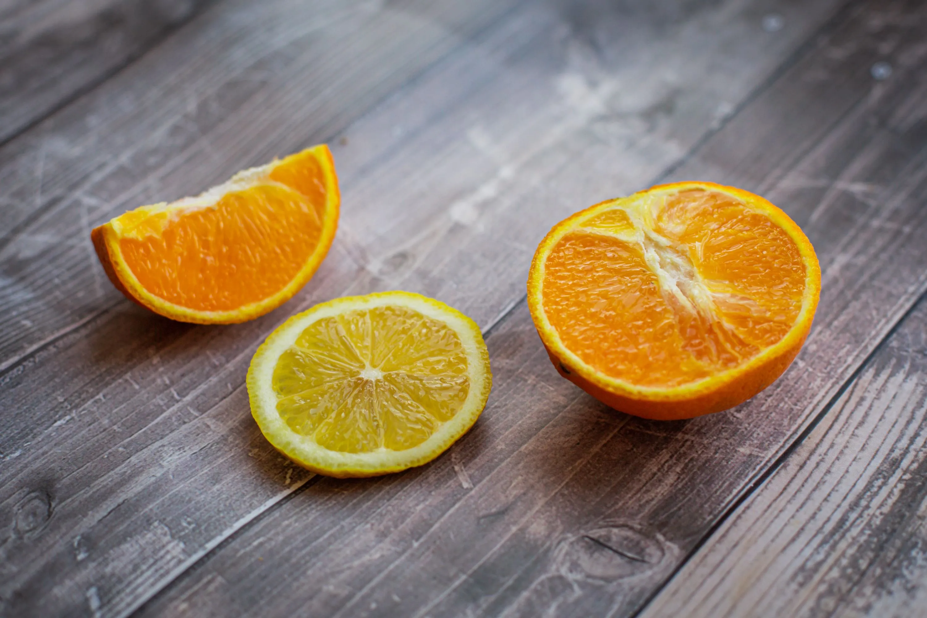 A sliced orange, an orange wedge, and a lemon slice on a wooden table, representing the citrus smell of loneliness.