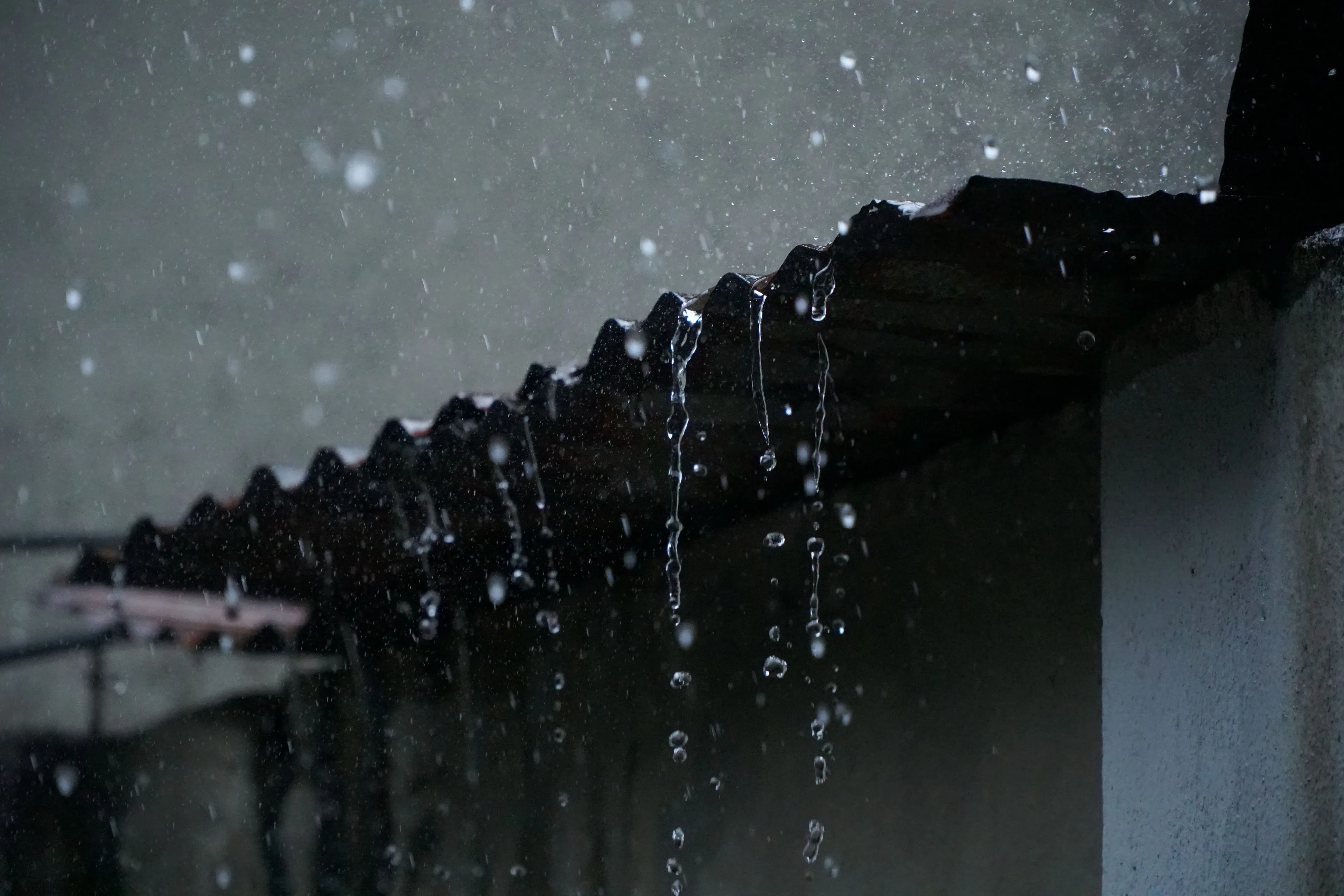 Rain falling from a corrugated roof, with water dripping down, symbolizing the smell of loneliness.