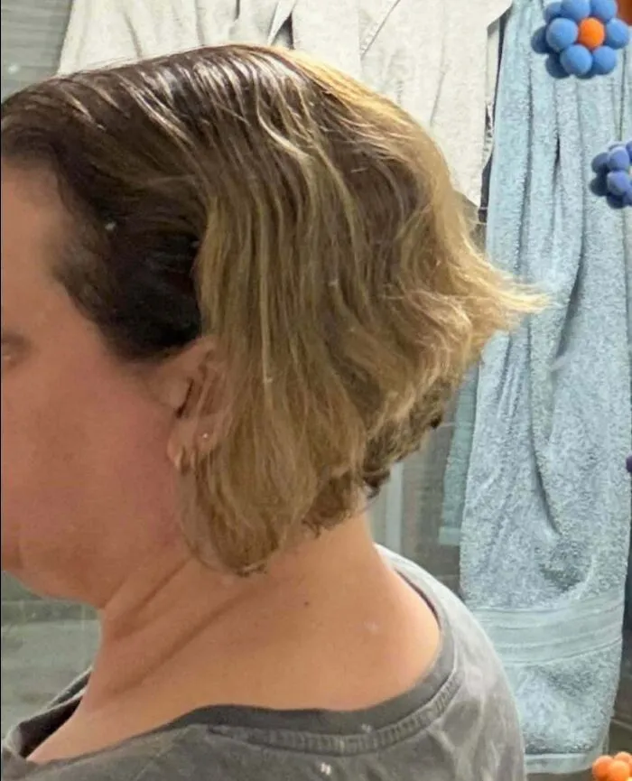 A woman with short, wavy, light brown hair looking at hair salon disasters, showing a bad haircut from the side.