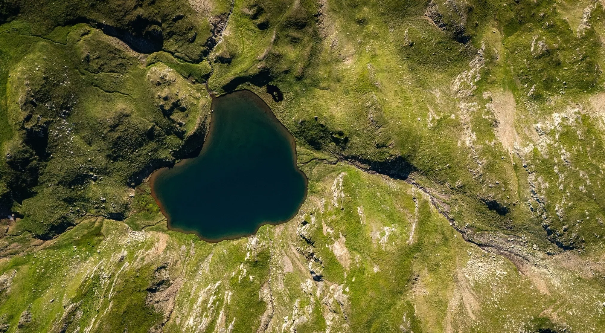 Aerial view of a dark blue lake nestled among lush green mountains, evoking the deepest lake in Europe.