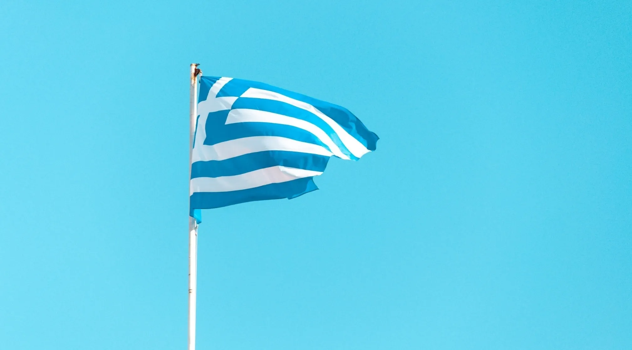 Greek flag waving against a clear blue sky, evoking General Knowledge About Europe and currency used in Greece before the euro.