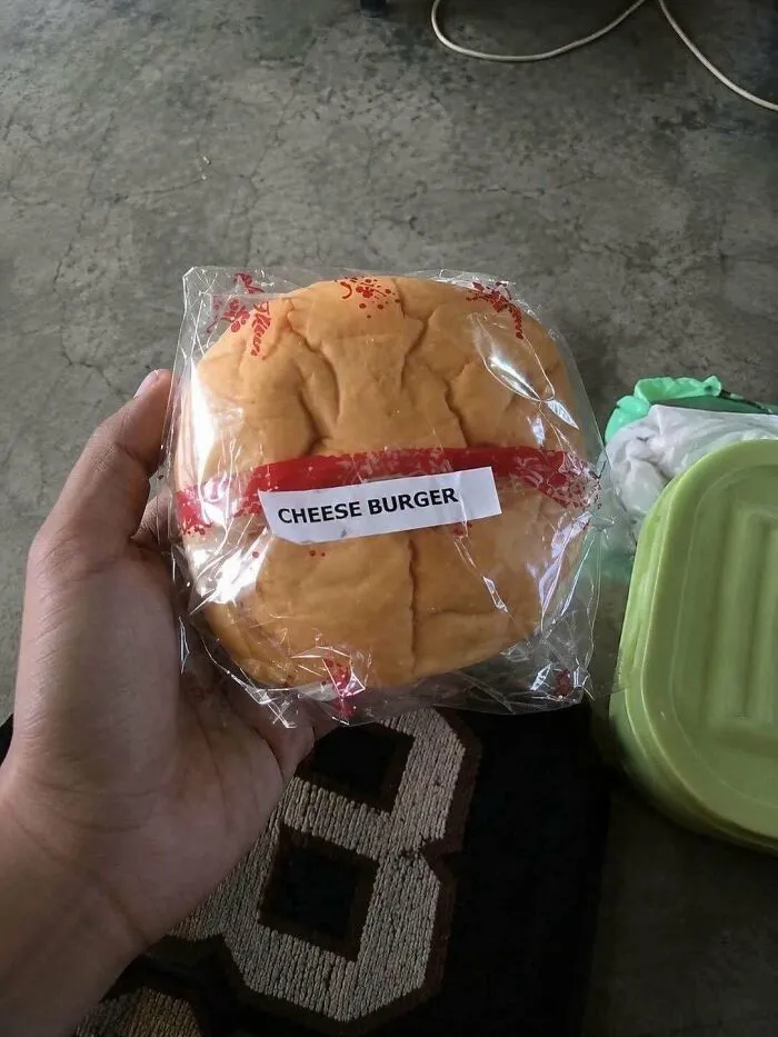A hand holding a packaged hamburger bun labeled Cheese Burger, representing a questionable food combo.