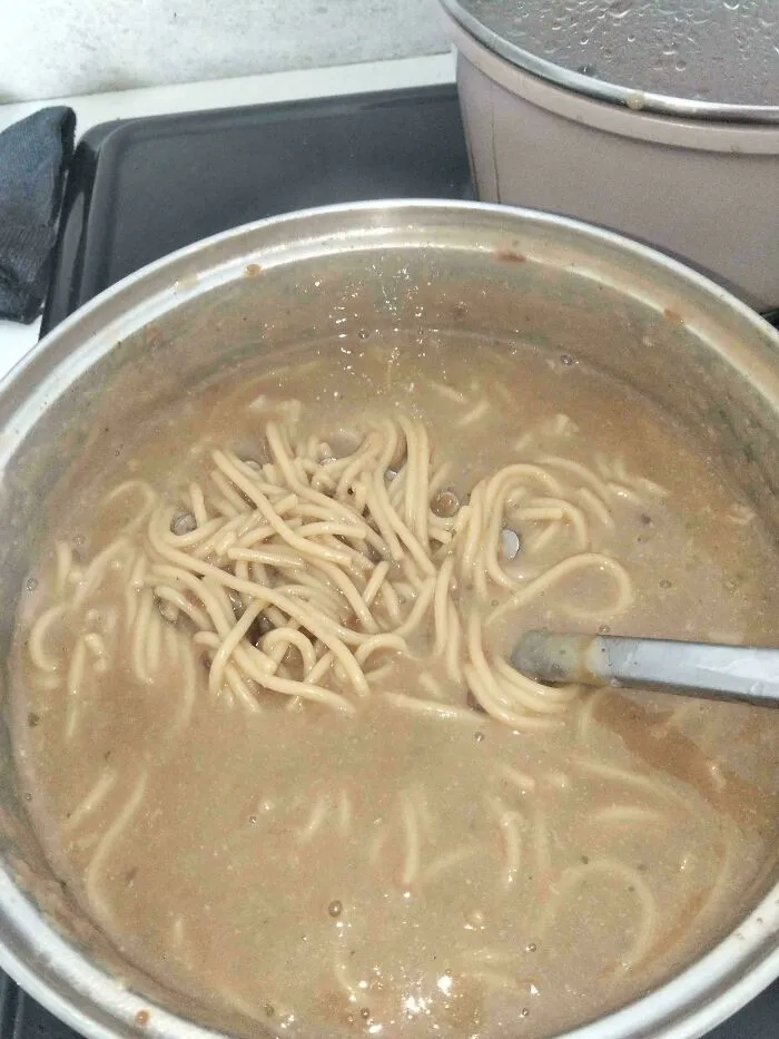 Spaghetti noodles submerged in brown broth inside a pot, showcasing a questionable food combo.