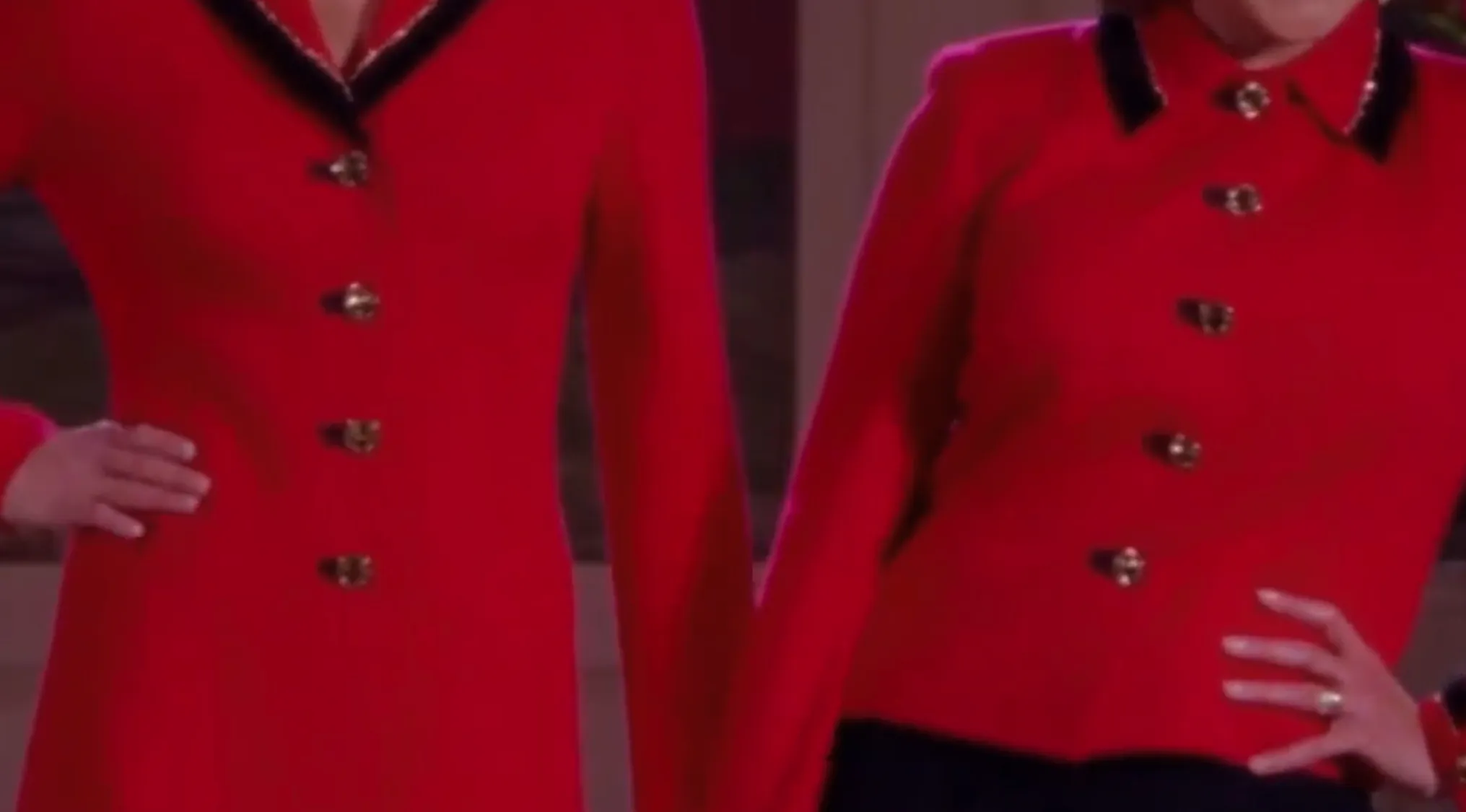 Two people in matching red TV show outfits with black lapels and ornate gold buttons.