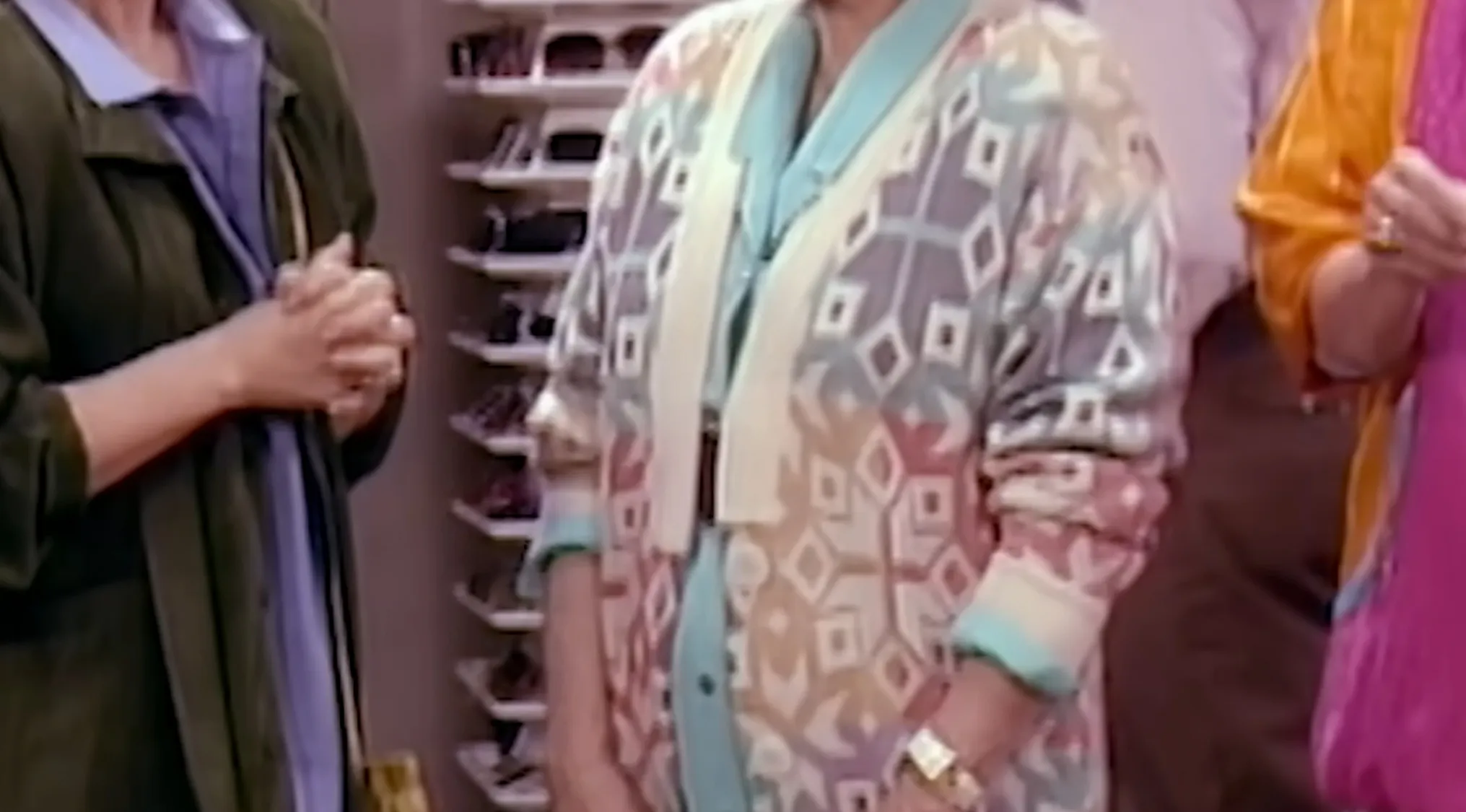 A woman wearing a colorful patterned cardigan, a light blue shirt, and a gold watch, showcasing distinctive TV show outfits.