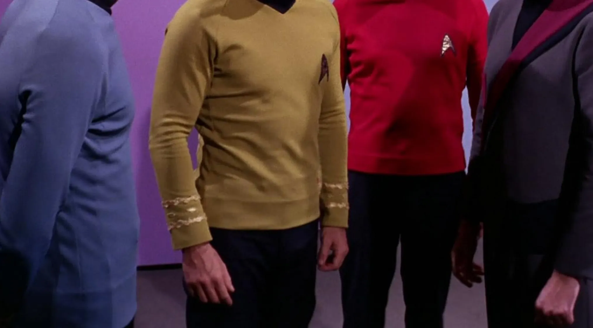 Four men in iconic minimalist TV show outfits, featuring a blue uniform, a gold uniform with embroidered cuffs, a red uniform, and a dark uniform with a red sash.