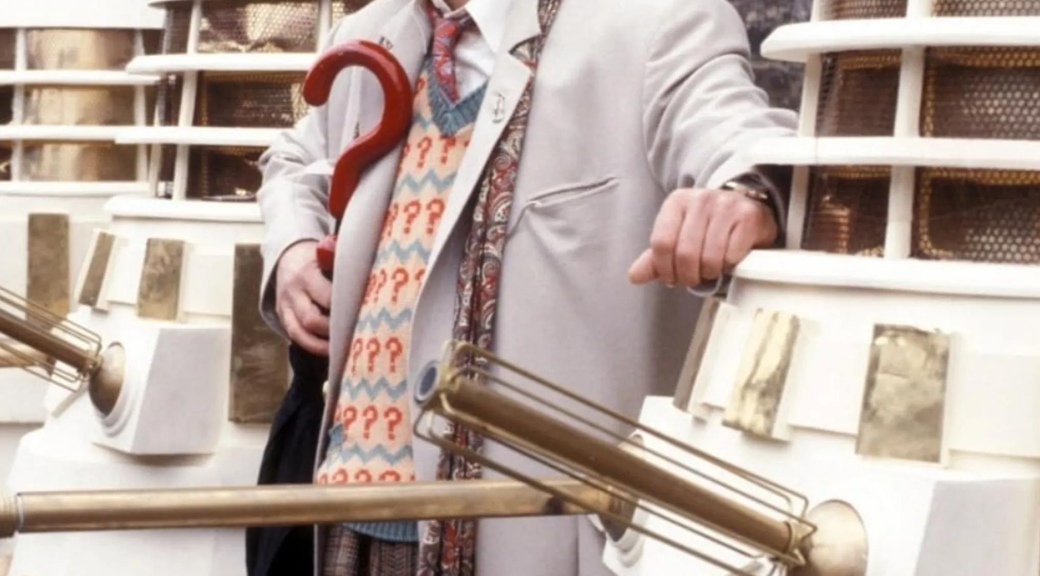 Close-up of a TV show outfit, featuring a beige jacket, patterned tie, and question mark sweater.