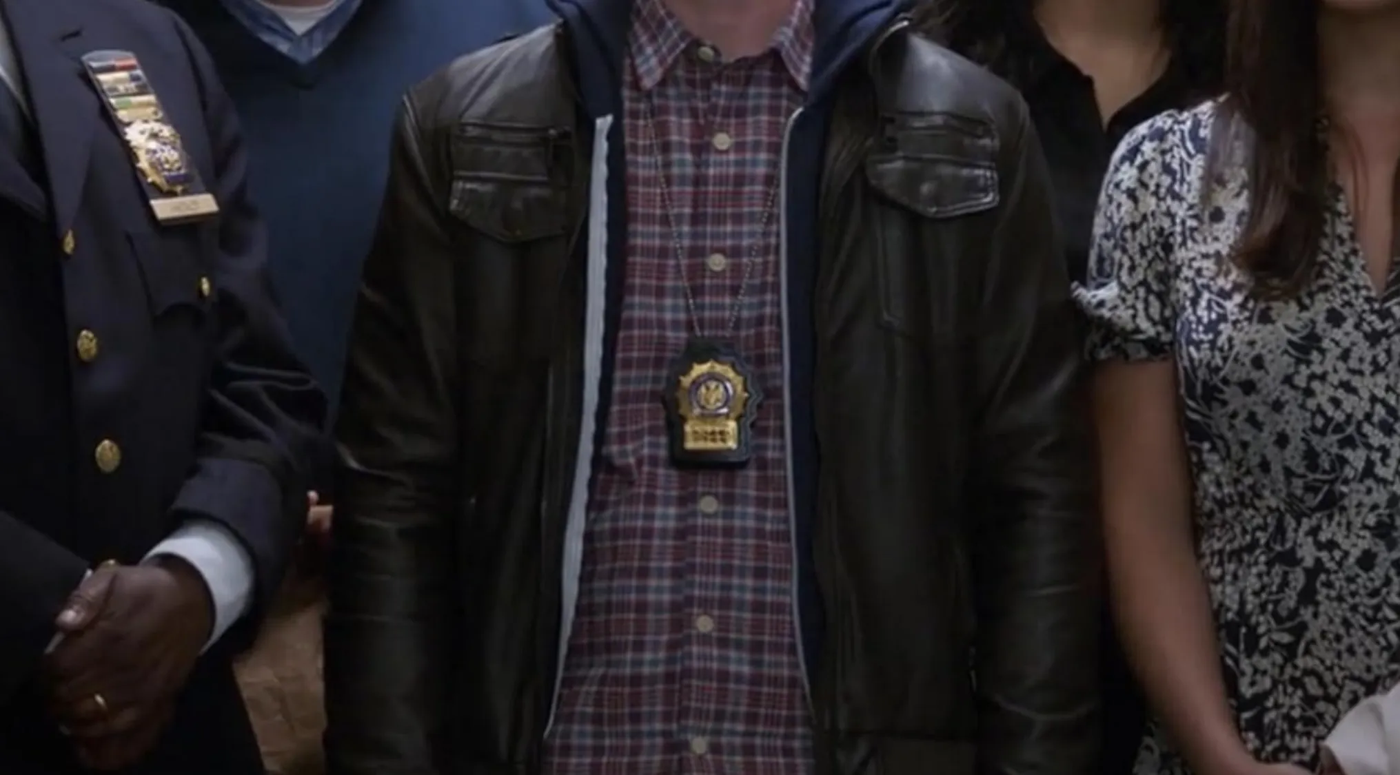 Close-up of a TV show outfit, featuring a brown leather jacket, plaid shirt, and police badge.