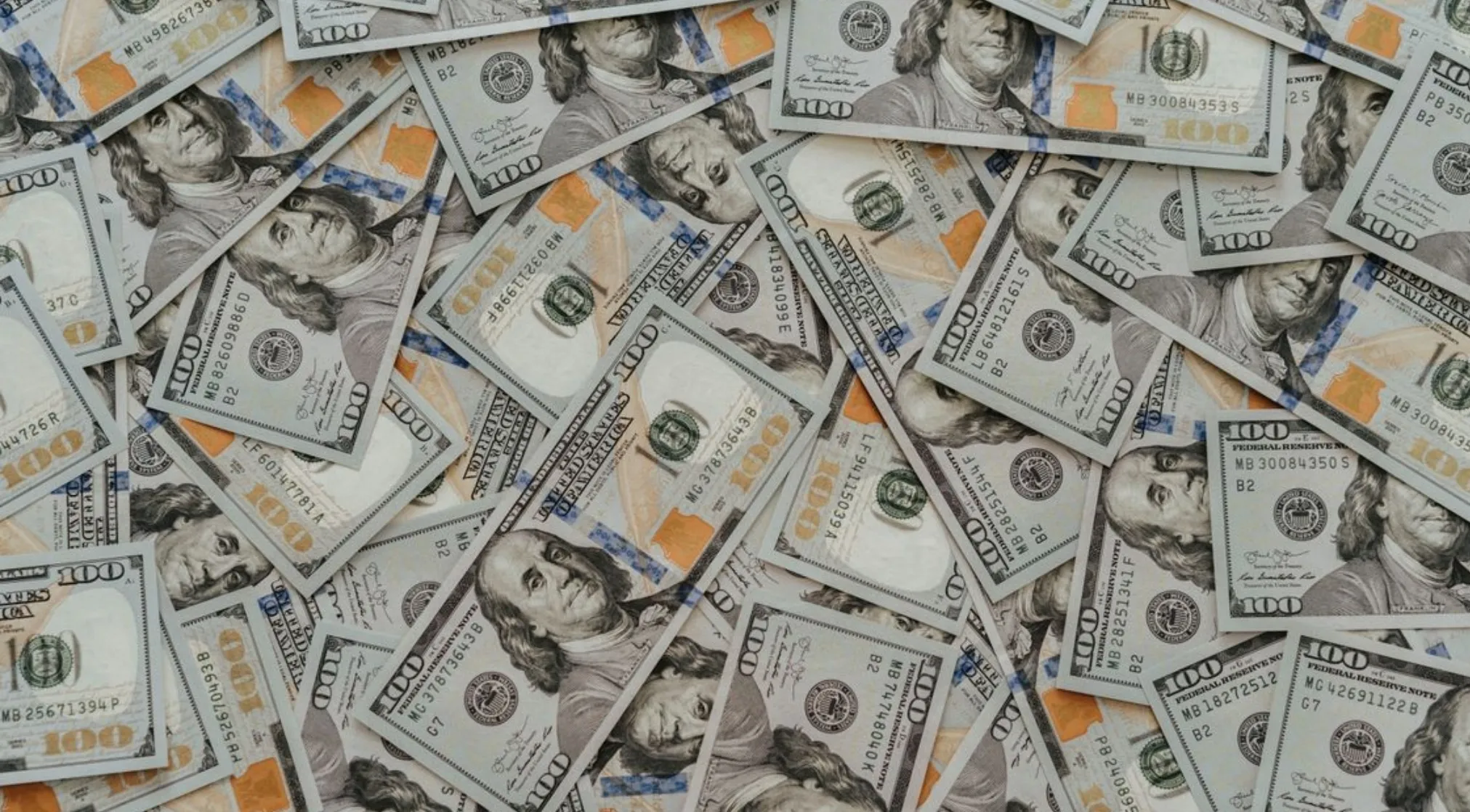 A large pile of scattered US hundred dollar bills. This visual represents wealth, useful for basic math concepts like how many hundreds.