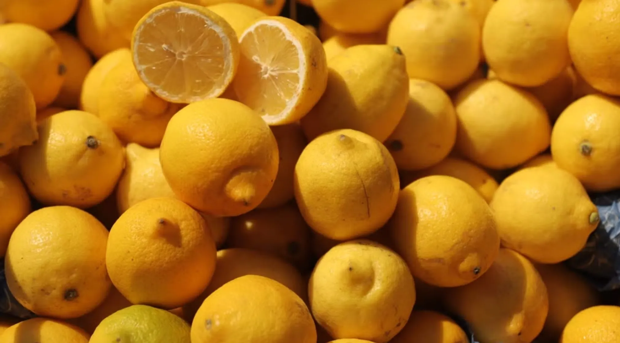 A pile of bright yellow lemons, with one cut in half, illustrating a basic math problem about packing lemons.