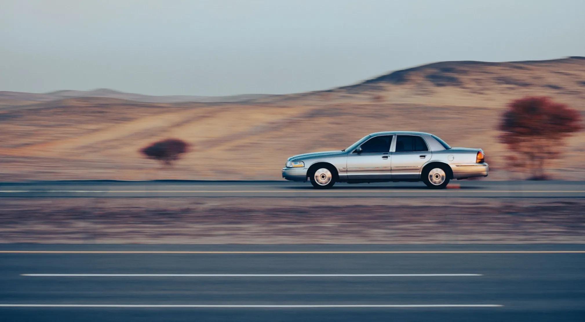 Silver car travels quickly on a highway with blurred desert landscape, applying basic math to solve distance problems.