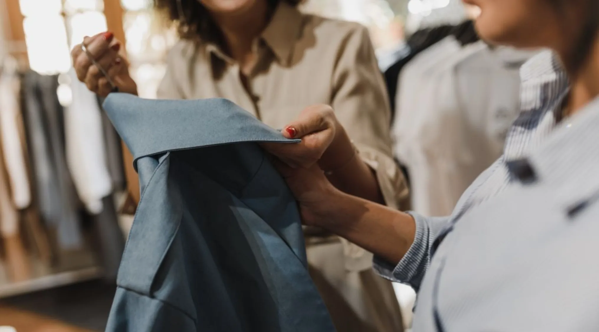Two women examine a blue jacket. One holds the sleeve, the other the collar. Relates to basic math and sale price.