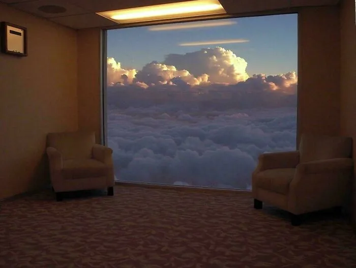 Two armchairs in a room with a window overlooking a vast expanse of clouds, an unsettling liminal space.