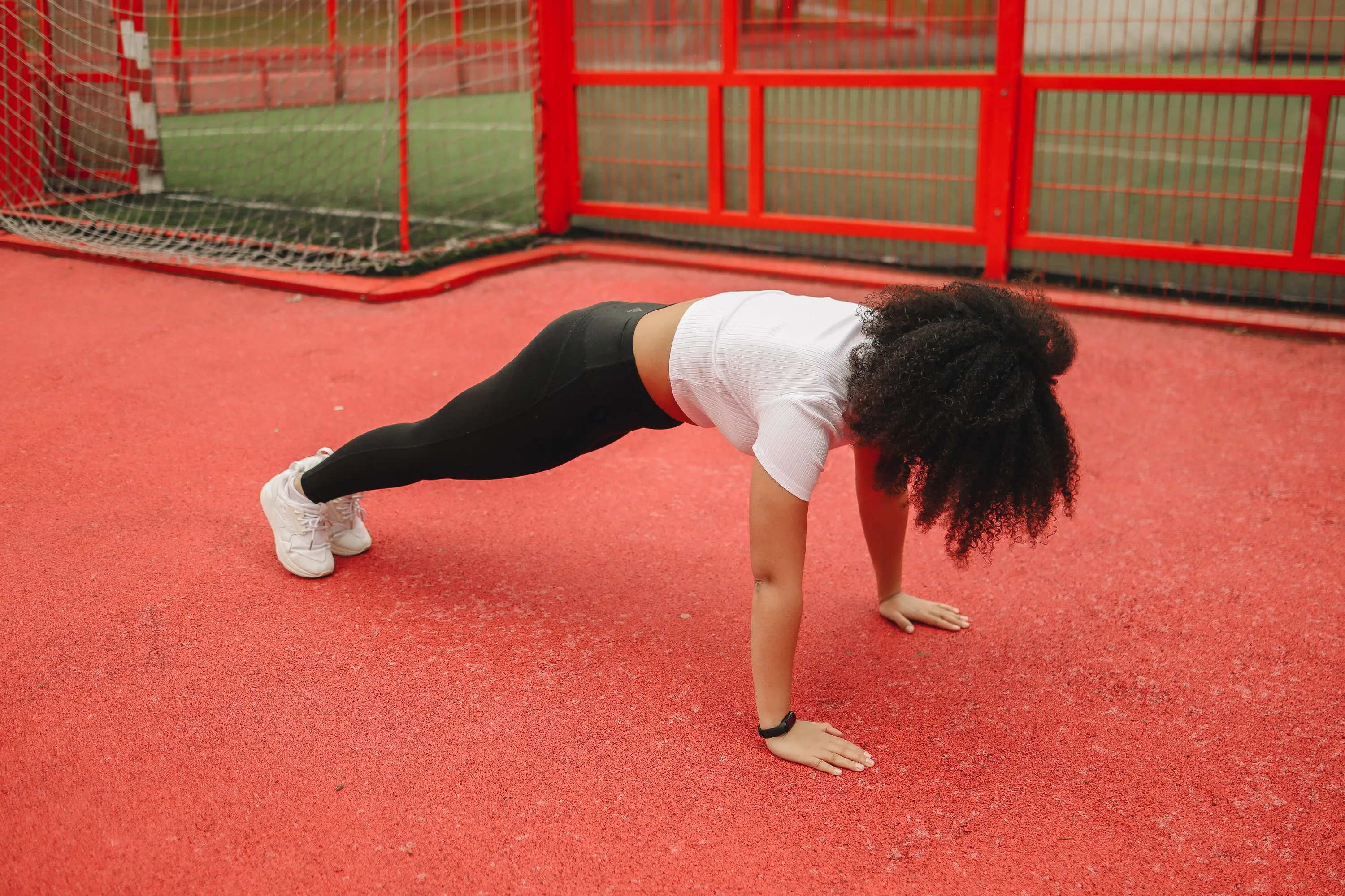 A woman with curly hair performing a solo workout plank on a red athletic court, embodying an ideal Saturday morning.