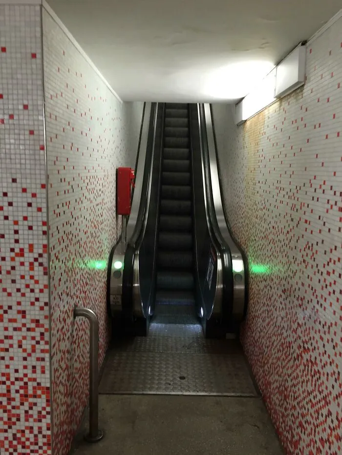 Deeply unsettling liminal space featuring a narrow escalator descending between red and white tiled walls.