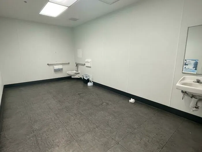 A bare, stark public restroom with a single toilet and sink, an unsettling liminal space.