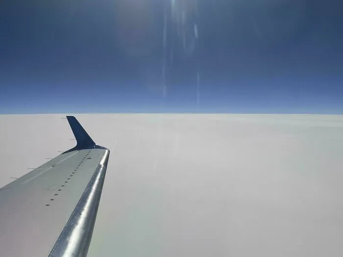 Airplane wing soaring above thick clouds, a deeply unsettling liminal space.