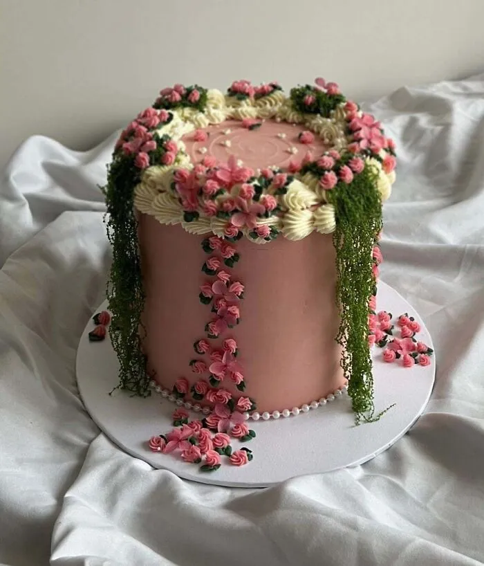 Pink floral cake decorated with cascading cream flowers and green leaves