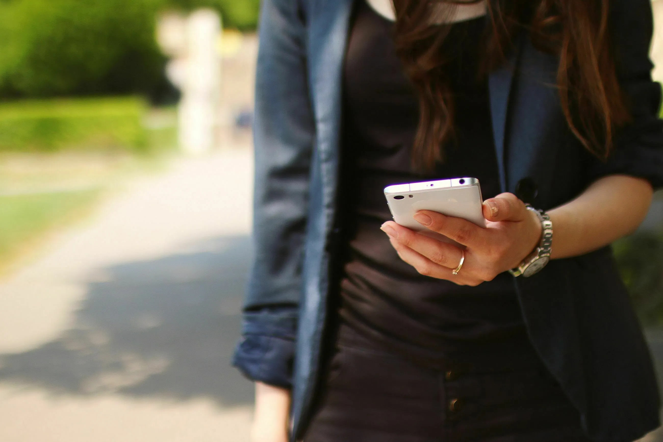 Woman holding a white smartphone, looking at a notification. What's your red flag? She's wearing a black top and a blue blazer.