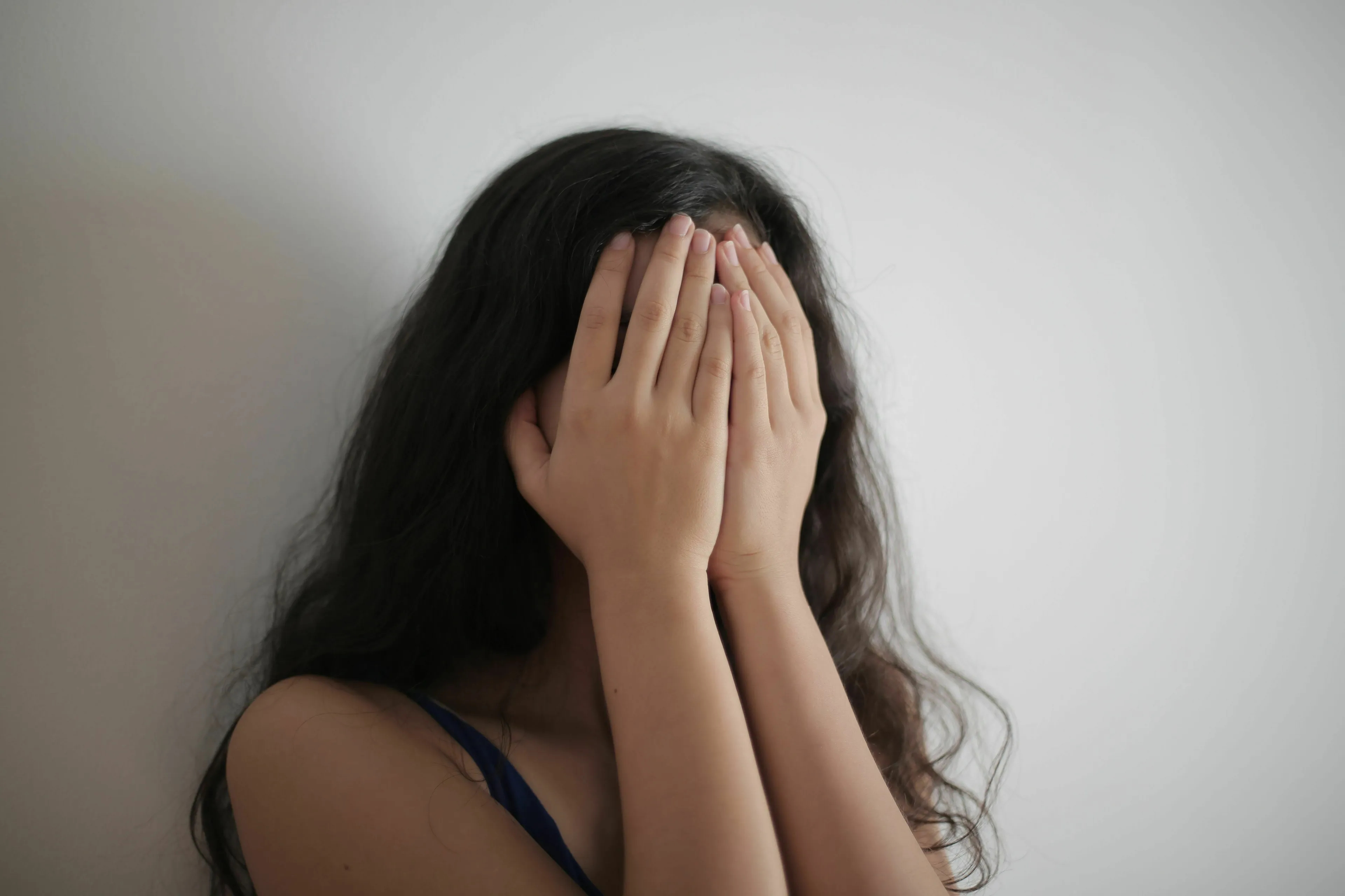 A person with long dark hair covering their face with their hands, showing a possible Red Flag reaction to a compliment.