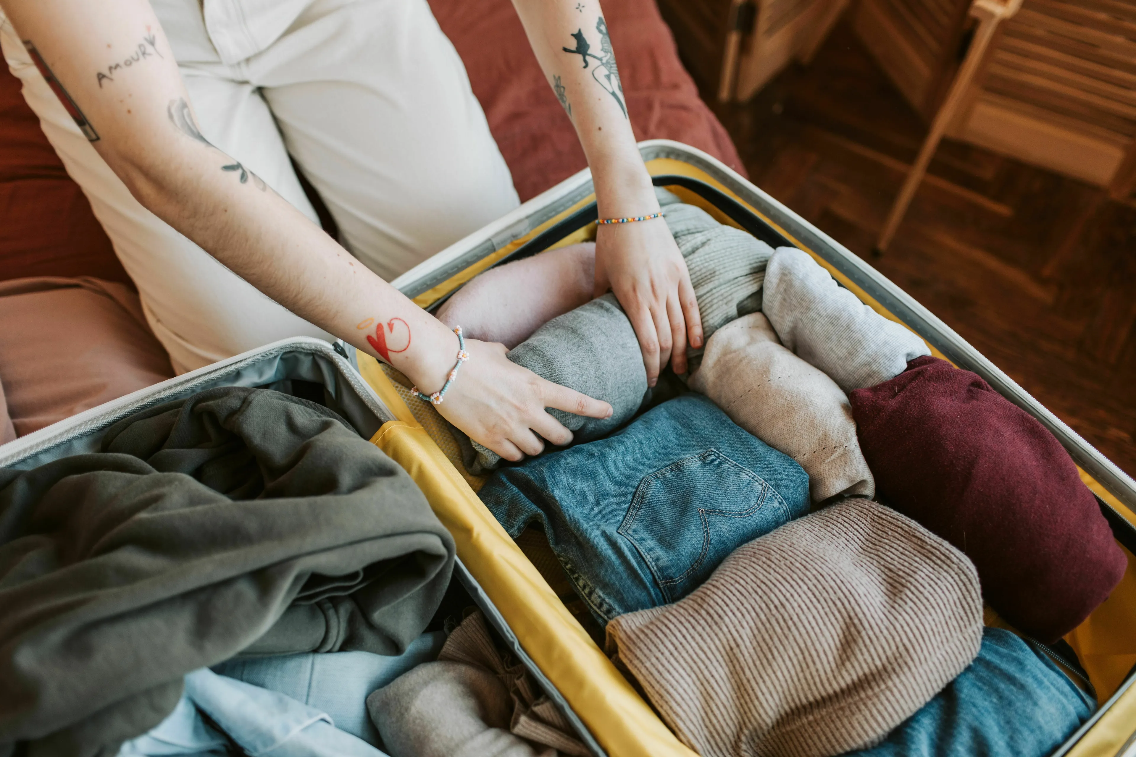 A person with tattoos on their arms neatly folding clothes into a suitcase, showcasing smart ways to pack for a trip.