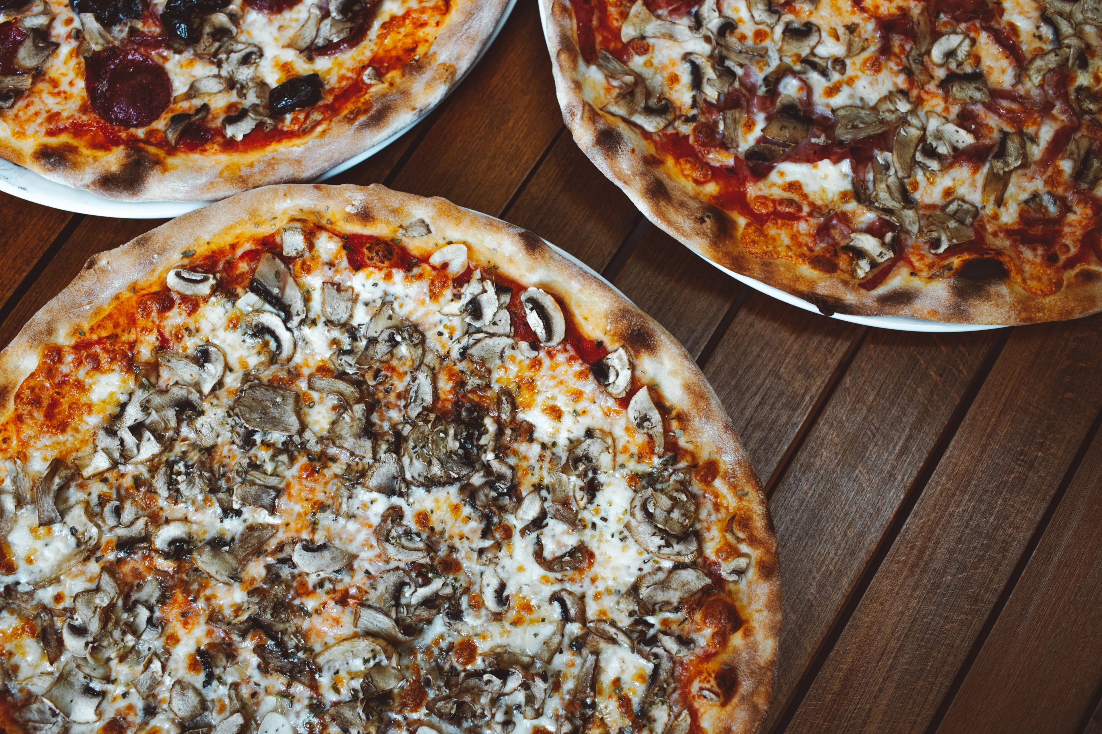Three delicious pizzas on a wooden table, one pepperoni and two mushroom, perfect comfort food.
