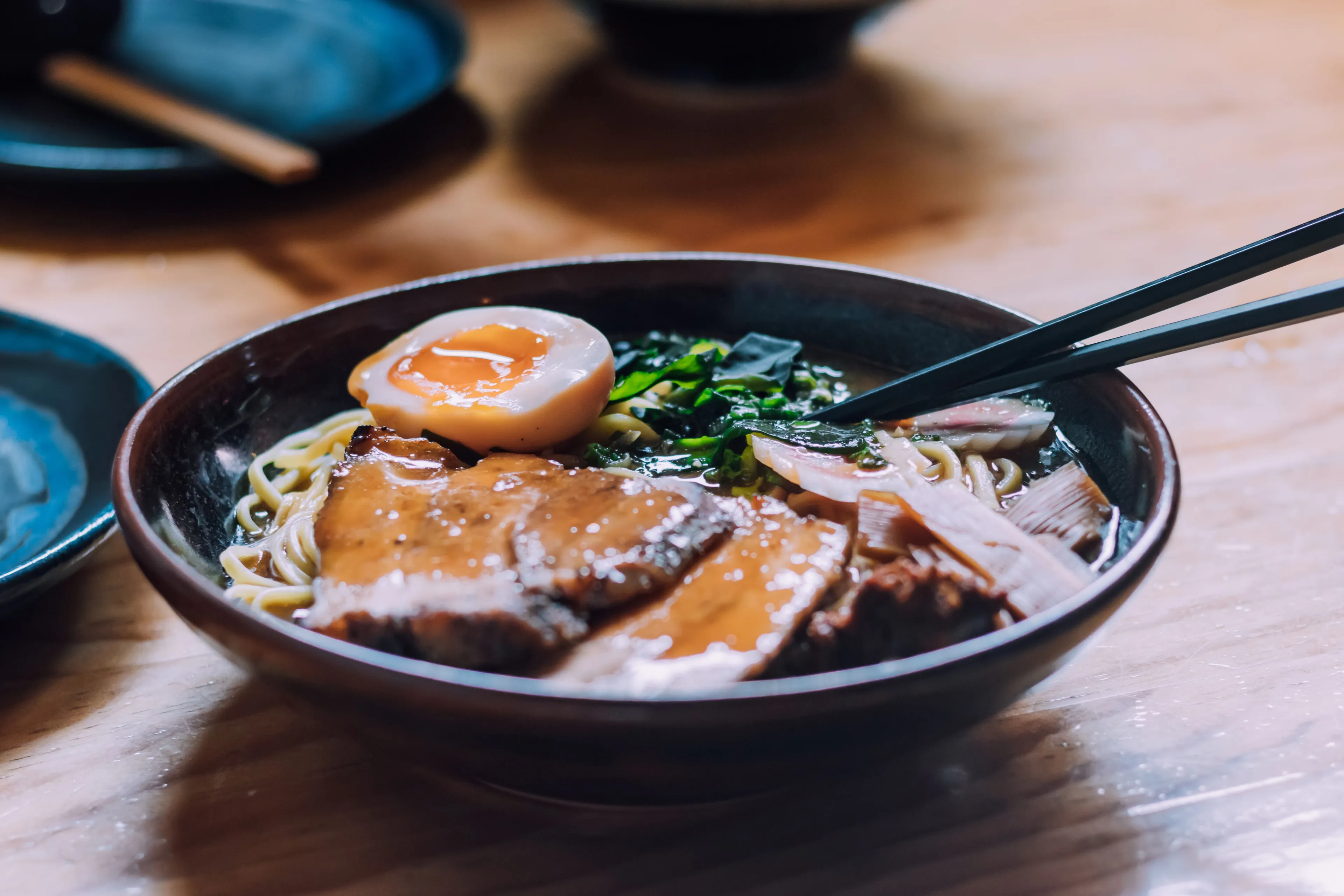 A close-up of a delicious bowl of ramen with noodles, sliced pork, a soft-boiled egg, and chopsticks.