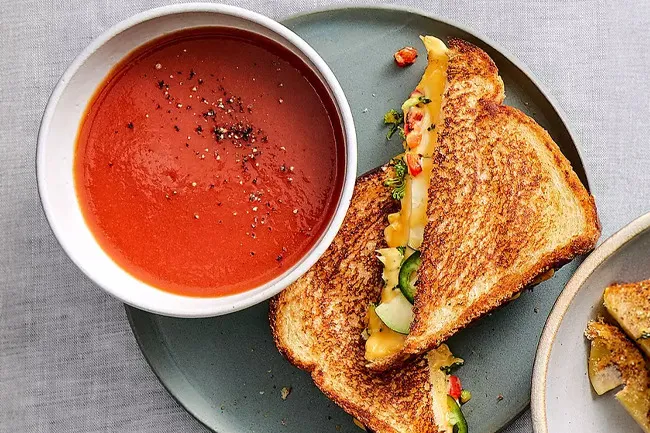 Grilled cheese and tomato soup, a classic comfort food, served with vibrant ingredients and a bowl of red soup.