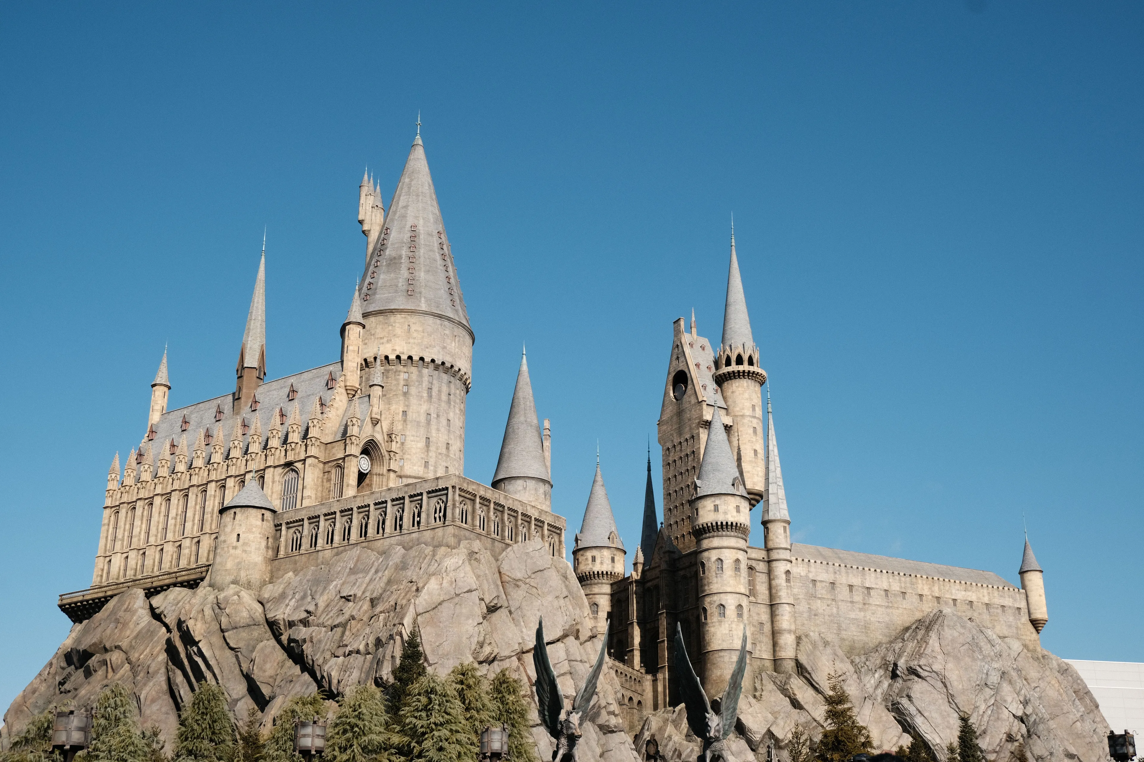 Hogwarts castle, a majestic and towering stone structure with many spires and turrets, stands proudly against a clear blue sky.