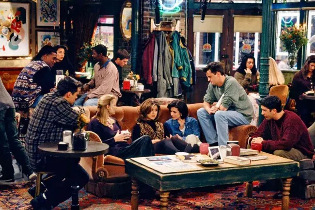 Friends cast at Central Perk, sitting on a couch and chairs, chatting in the coffee shop, a fictional place to live.