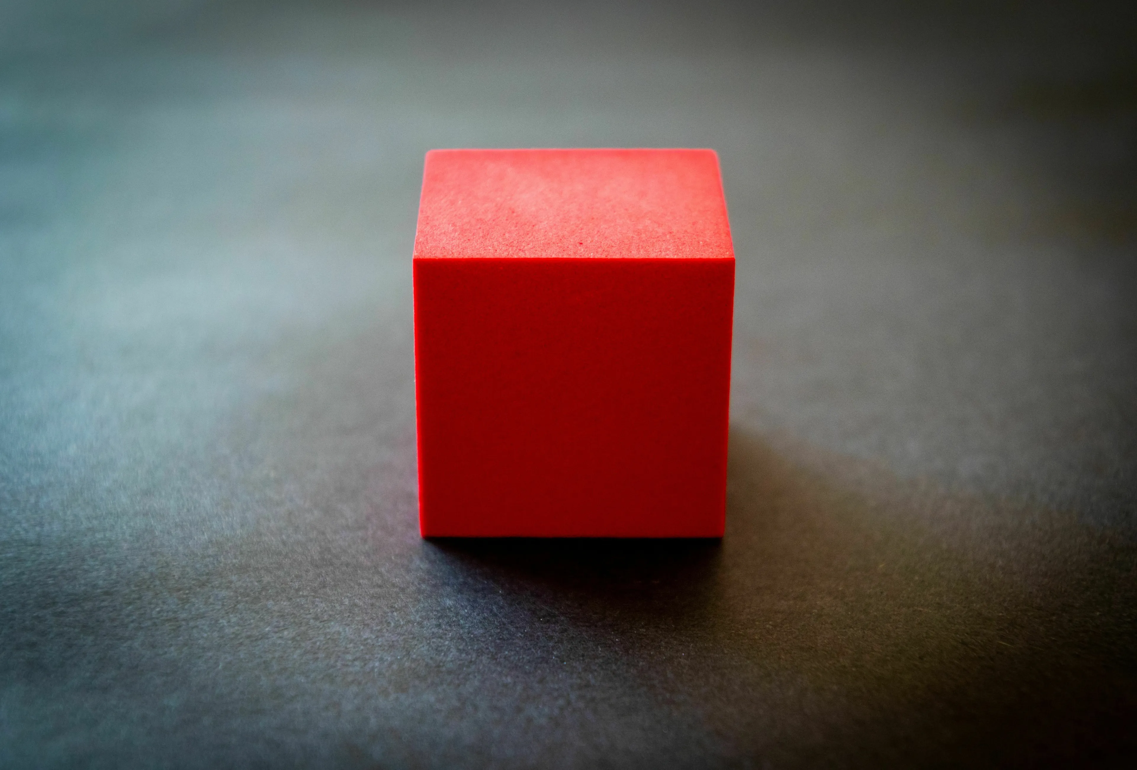 A red cube on a dark surface, highlighting the geometric shape for general knowledge; how many edges does a cube have?