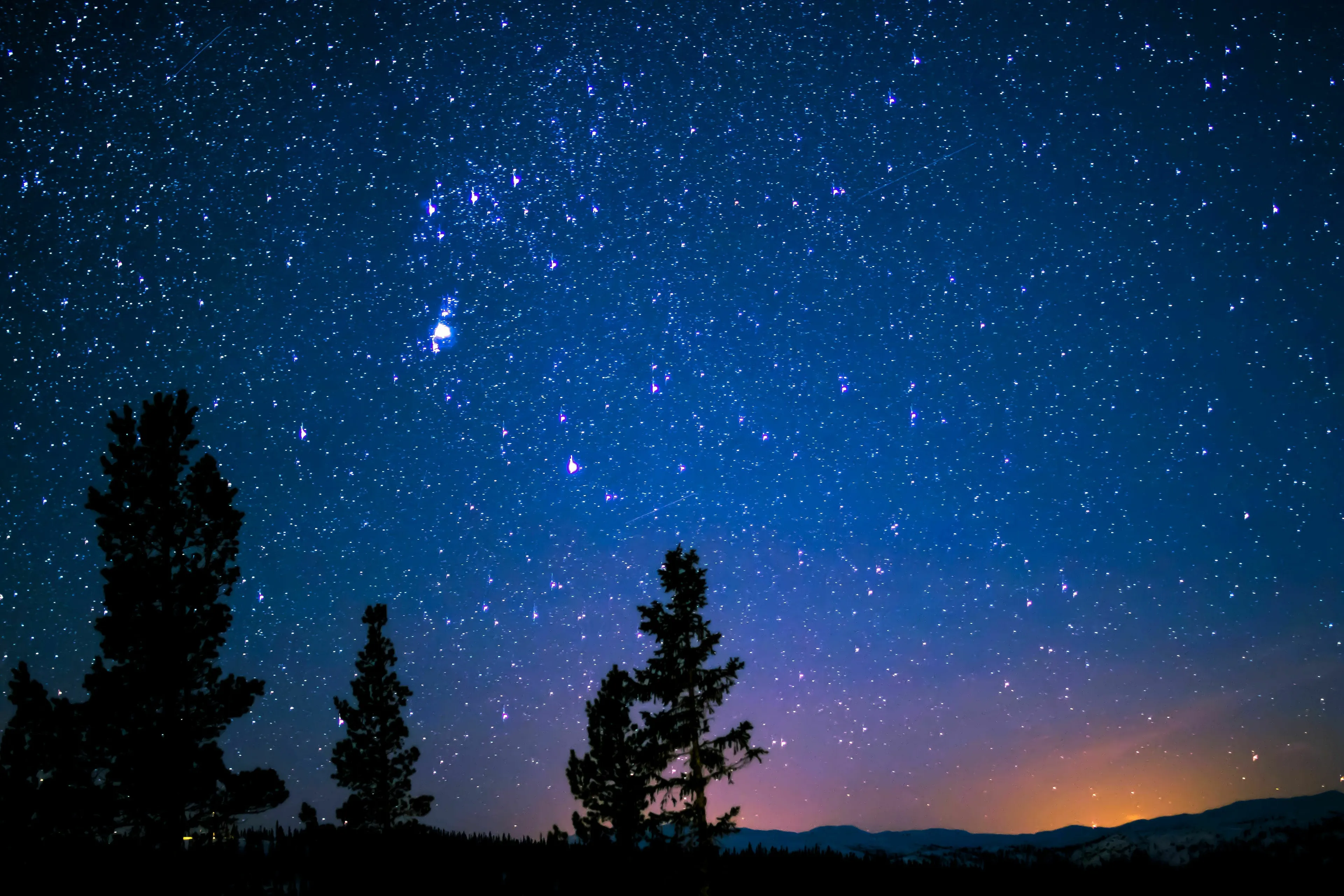 A beautiful starry night sky with numerous constellations visible above silhouetted trees and mountains.