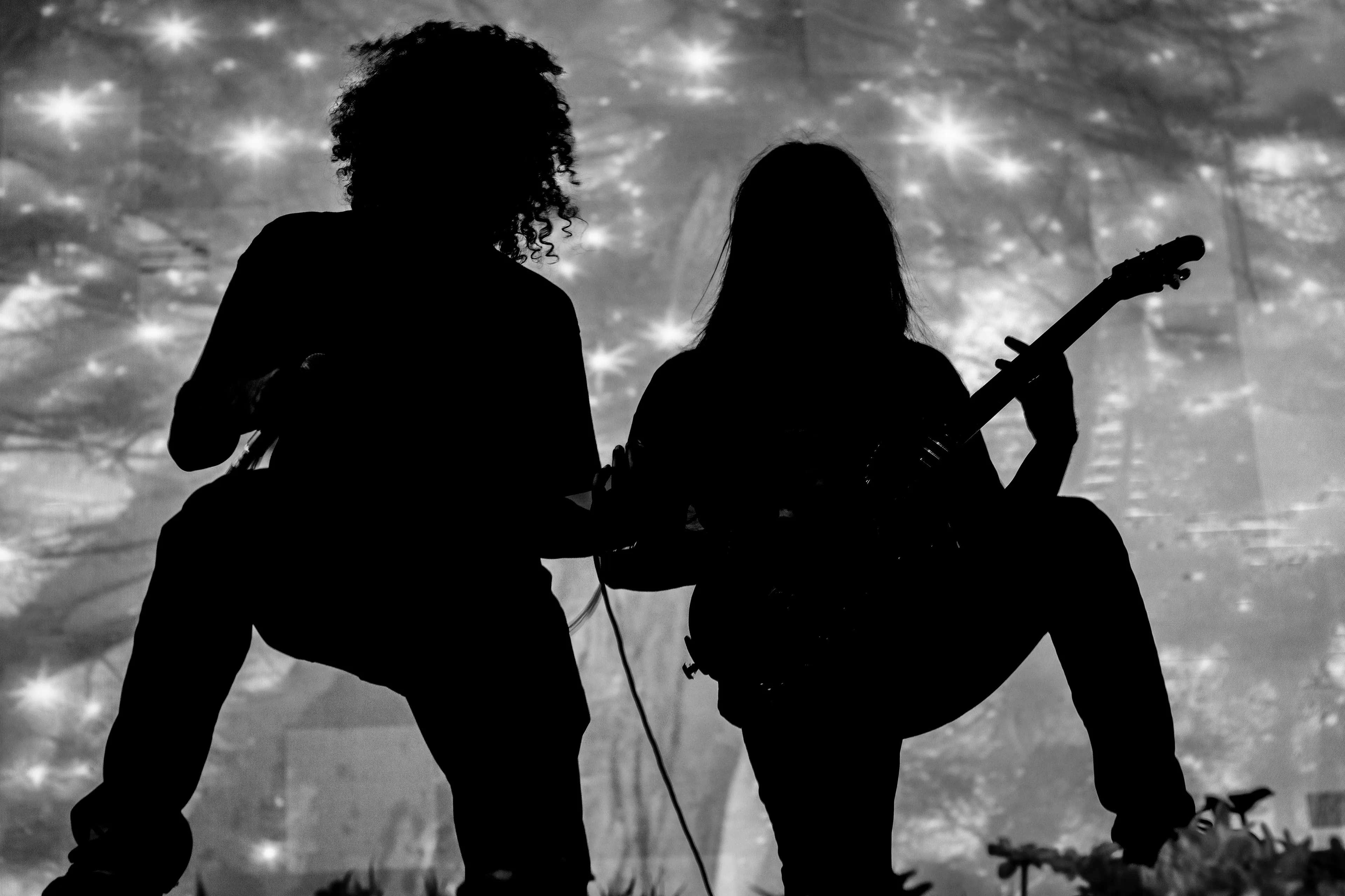 Silhouettes of two musicians, one playing a bass guitar, against a starry background. General Knowledge about bass guitar strings.