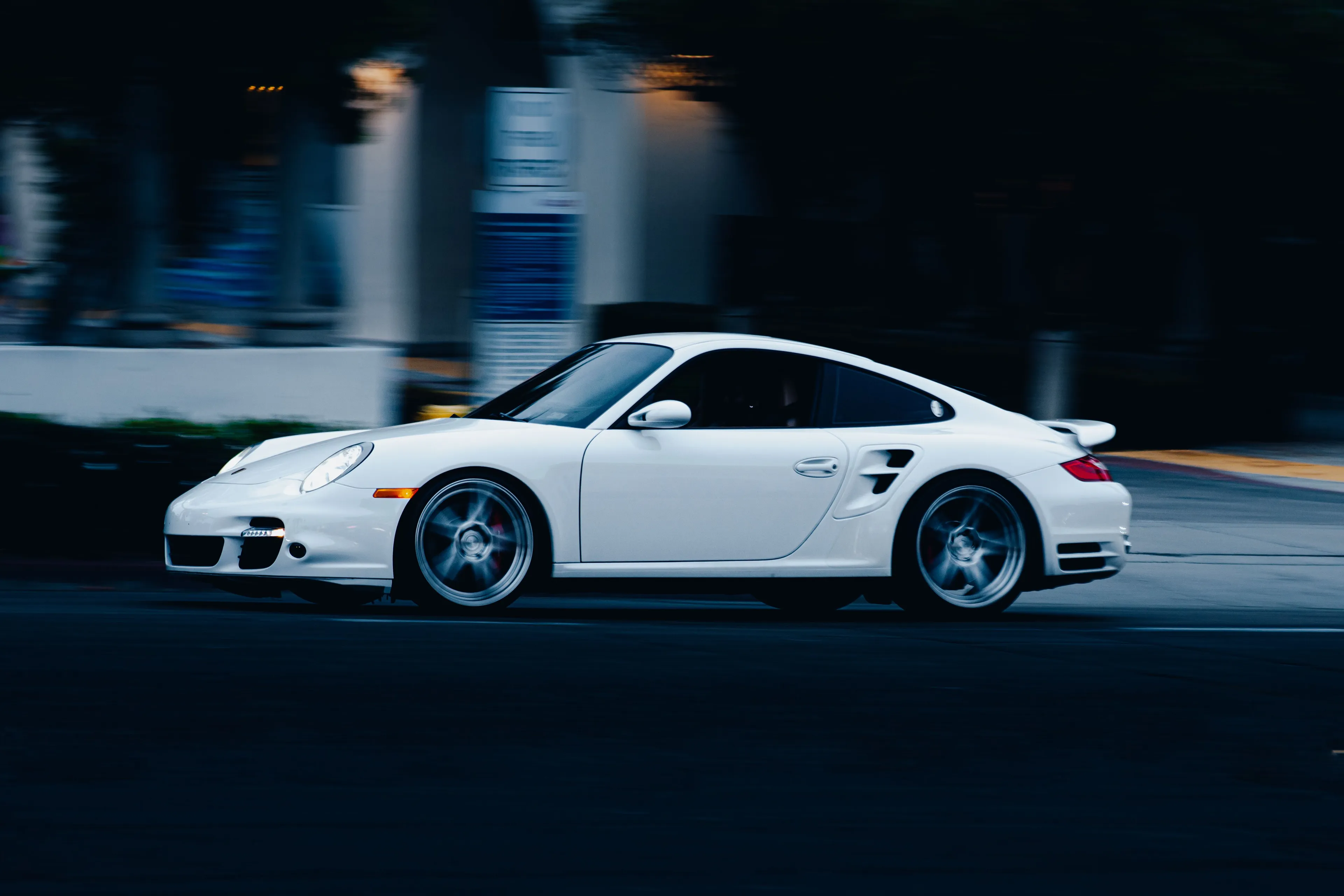 A white Porsche sports car in motion, blurring the background, with spinning wheels on a dark road.